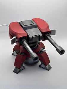 "Image of a 3D Printed Torbjörn Turret Replica from Overwatch in motion. The replica turret is made of high-quality plastic and designed to look like the in-game version. The turret is shown with its signature orange and gray color scheme, and is in mid-rotation with its barrel pointed forward. This replica is perfect for Overwatch fans and collectors who want to add a realistic and unique item to their collection."